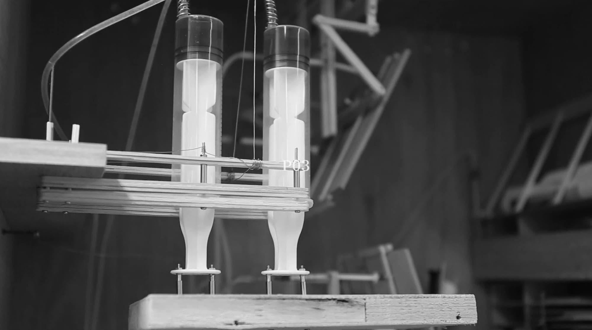 Video still — the twin syringes of parasite P03, charged with water, mounted on the wooden frame