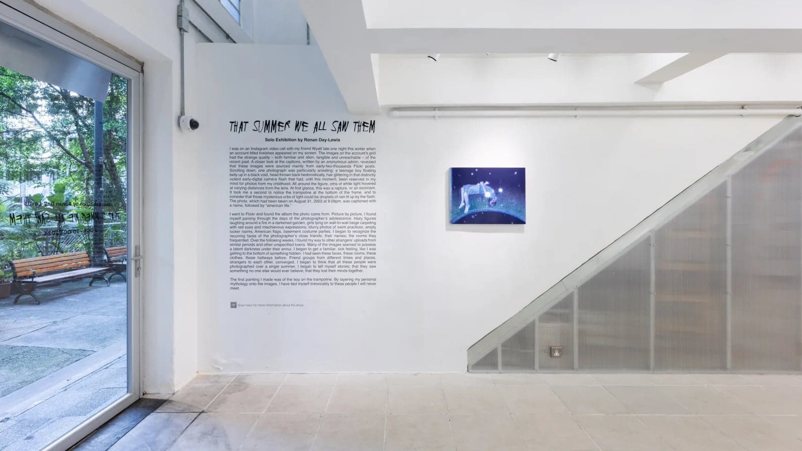 Exhibition text wall by the entrance, a single small canvas beside the polycarbonate under-stair enclosure