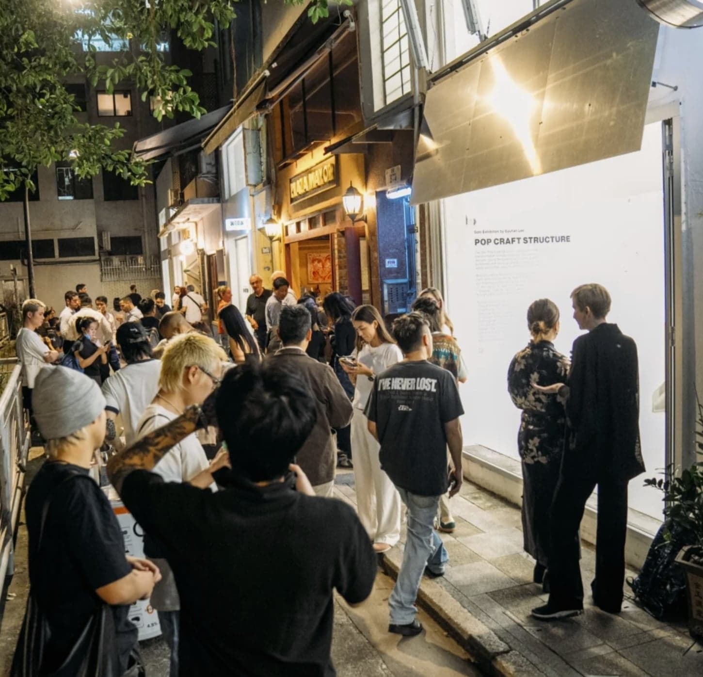 Opening night — the crowd filling the lane outside the lifted awning and glowing storefront